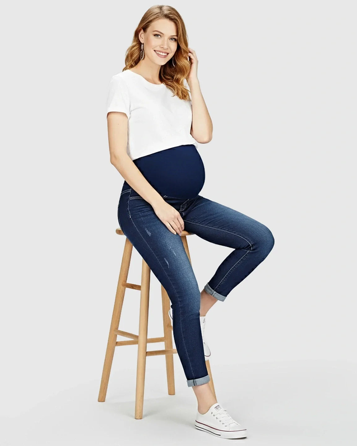 Smiling pregnant woman in full panel distressed maternity skinny jeans with a white tee.