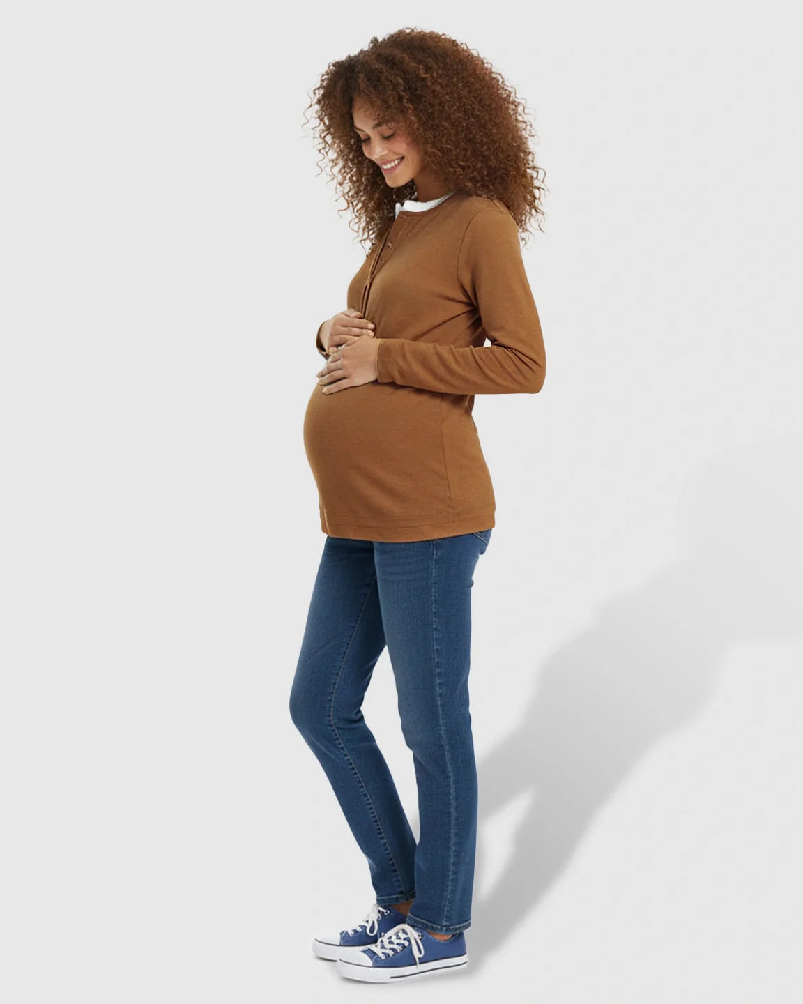 Pregnant woman in a brown long-sleeve henley maternity and nursing top with white trim and blue jeans.