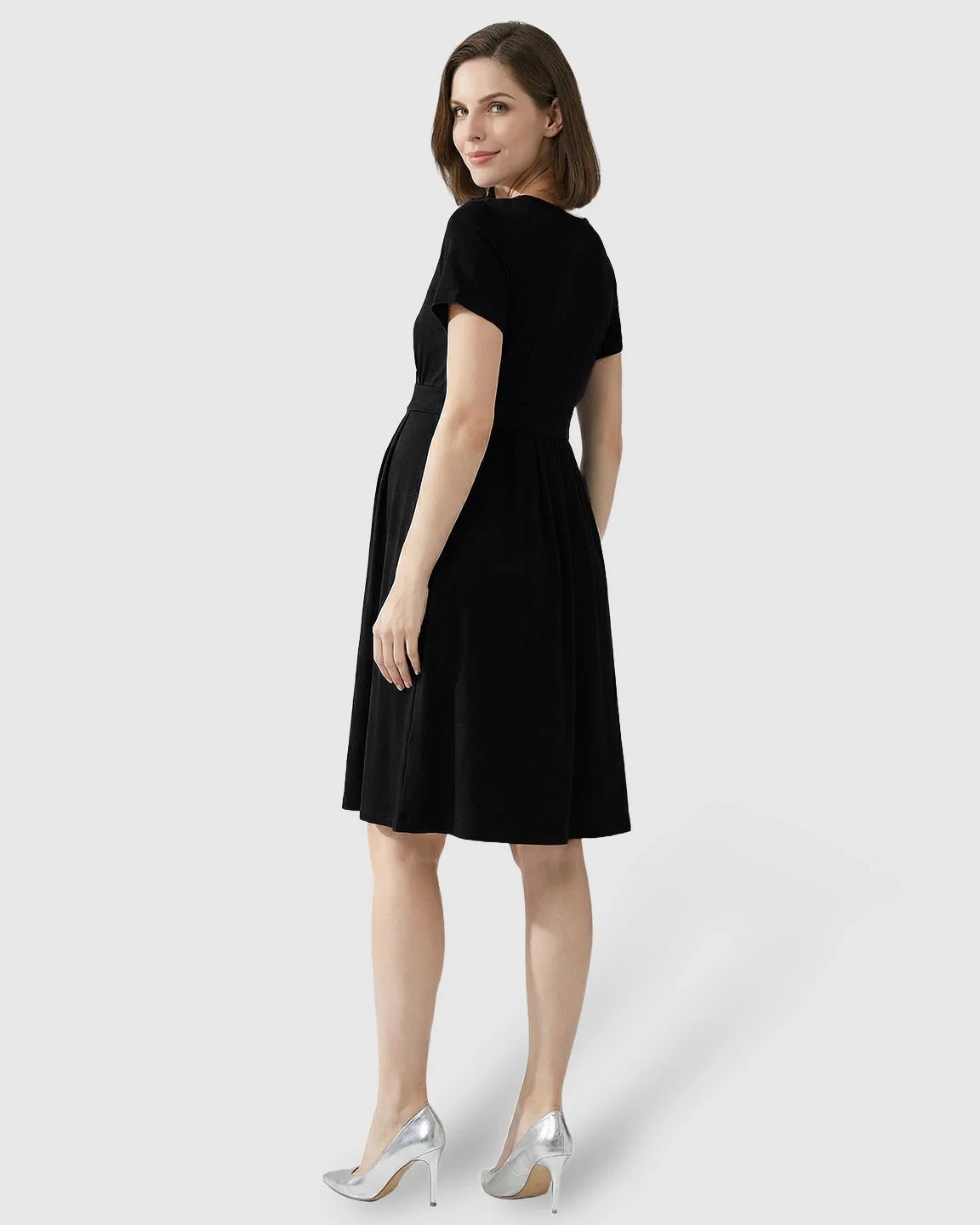Woman in a black V-neck A-line maternity and nursing dress with short sleeves, looking over her shoulder.