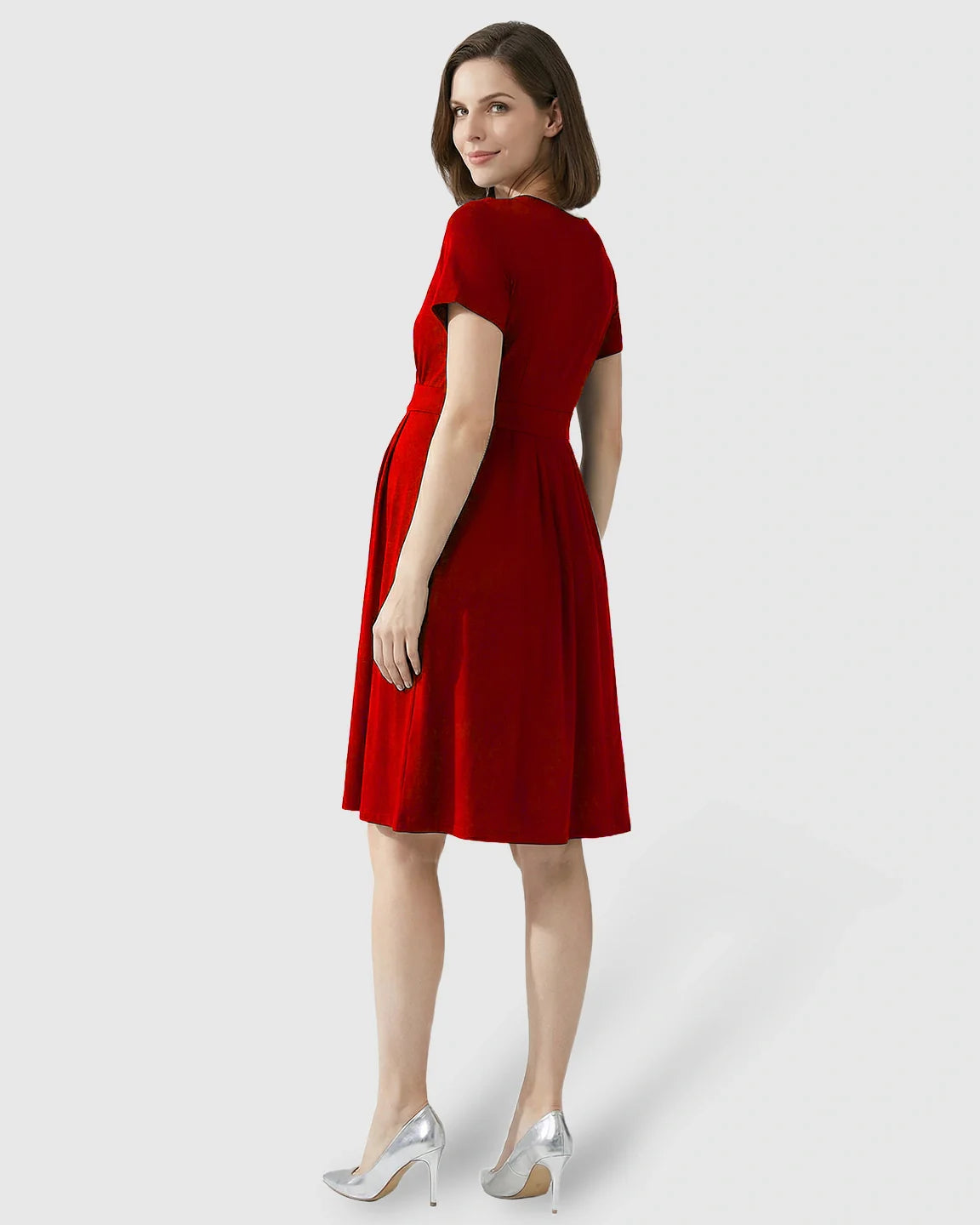 Woman in a red V-neck A-line maternity and nursing dress with short sleeves, looking over her shoulder.