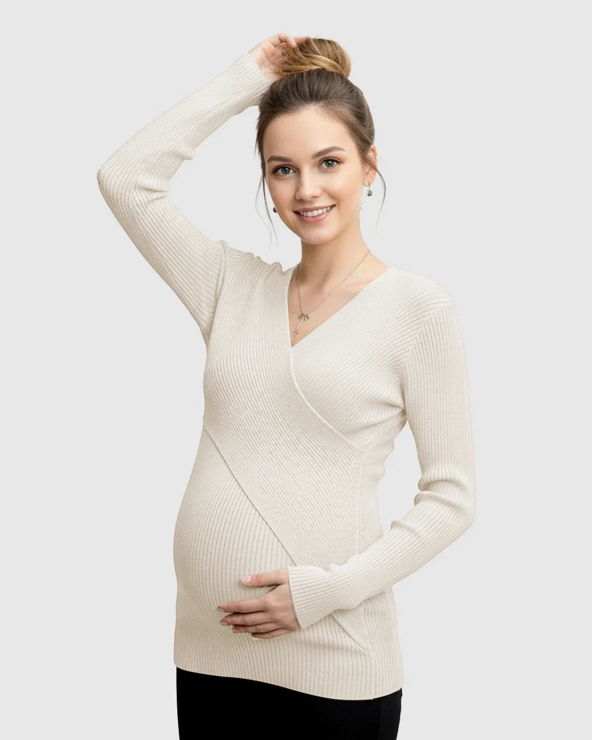 Pregnant woman in a cream faux-wrap ribbed maternity top, smiling and holding her bump.