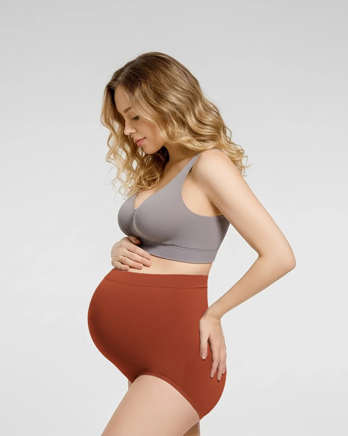 Pregnant woman modeling rust-colored, high-waist seamless maternity panties with a supportive design.