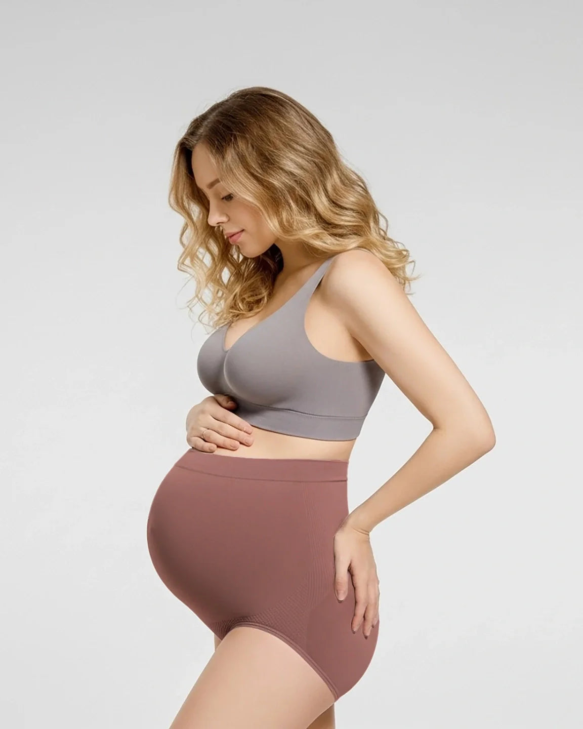Pregnant woman in a gray bra and high-waist seamless maternity panties in a dusty rose color.