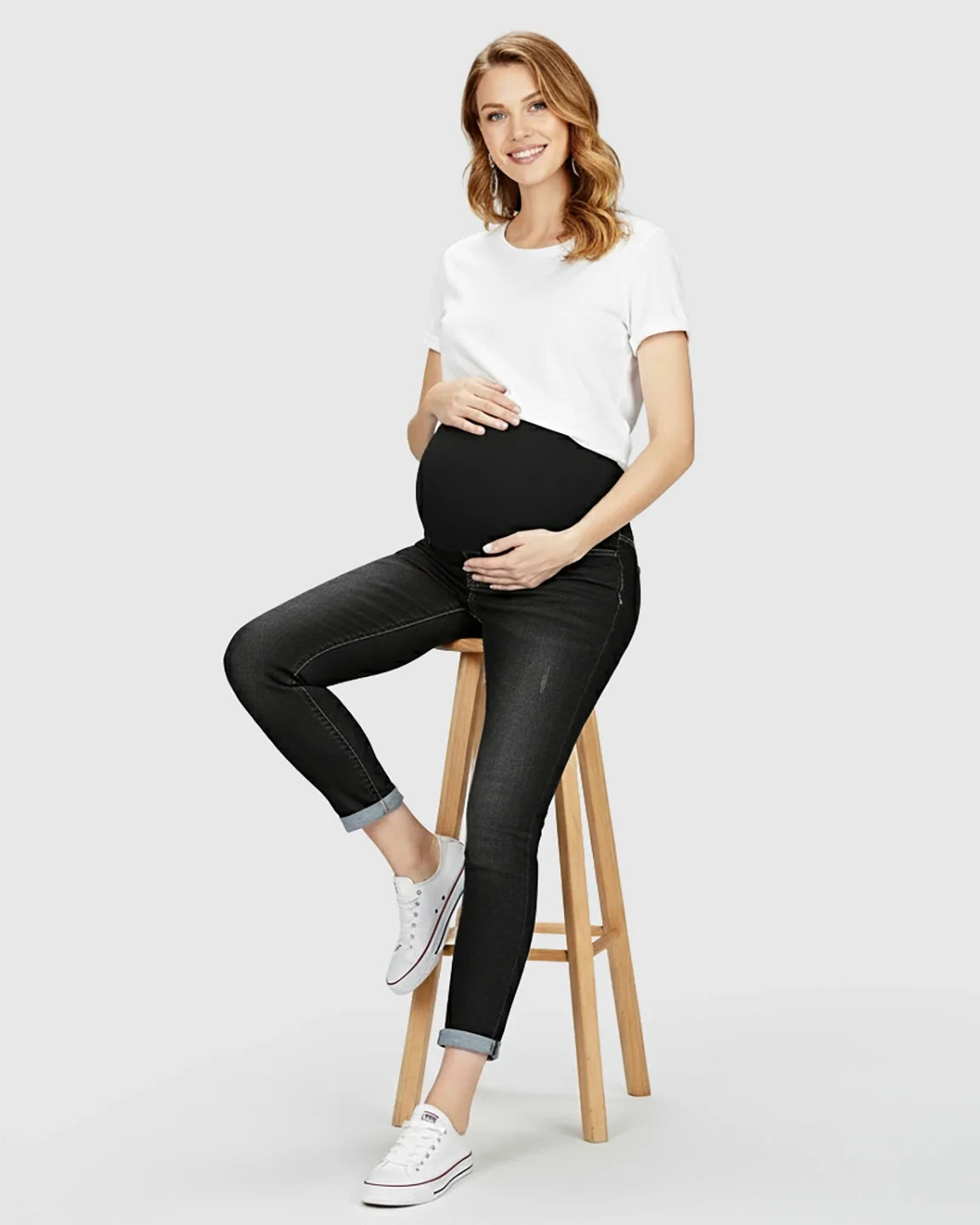 Smiling pregnant woman in black distressed maternity skinny jeans with full panel and white t-shirt.