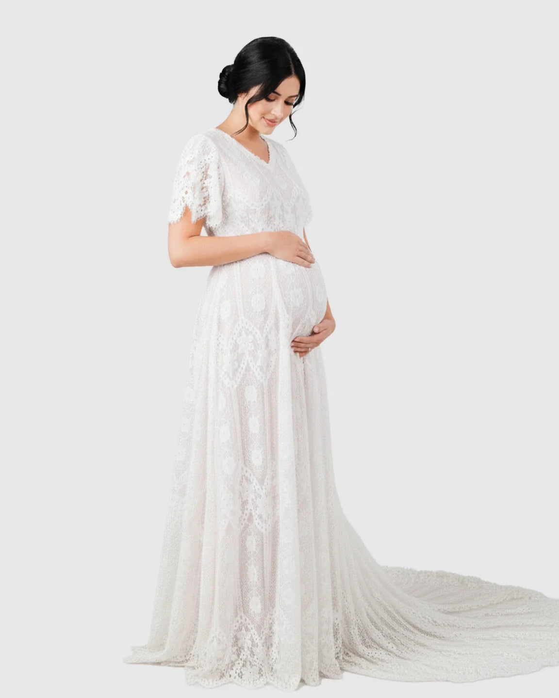 White vintage lace maternity gown with flutter sleeves, V-neck, and long trailing hem, highlighting a pregnant belly.