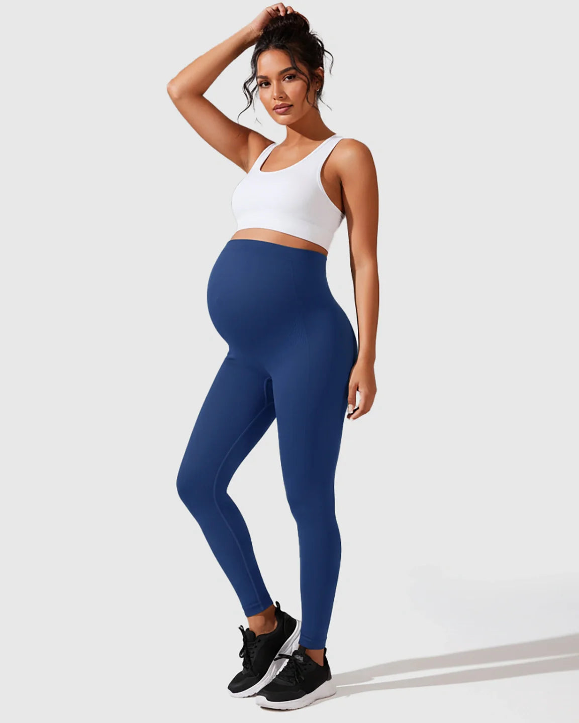 Pregnant woman in seamless navy blue M-shape maternity leggings and a white sports bra.
