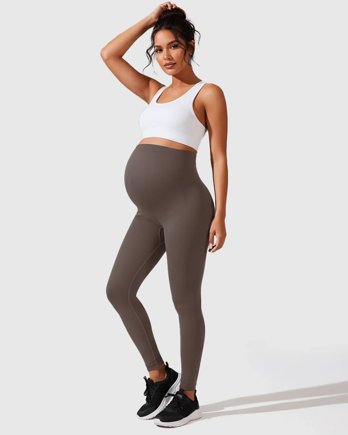 Woman in seamless, high-waisted gray maternity leggings and white sports bra, posing confidently.