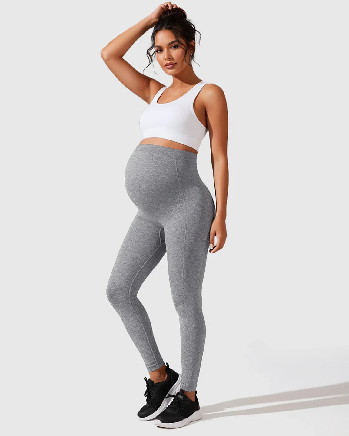 Woman models gray seamless M-shape maternity leggings with a white sports bra, showcasing full-belly support.