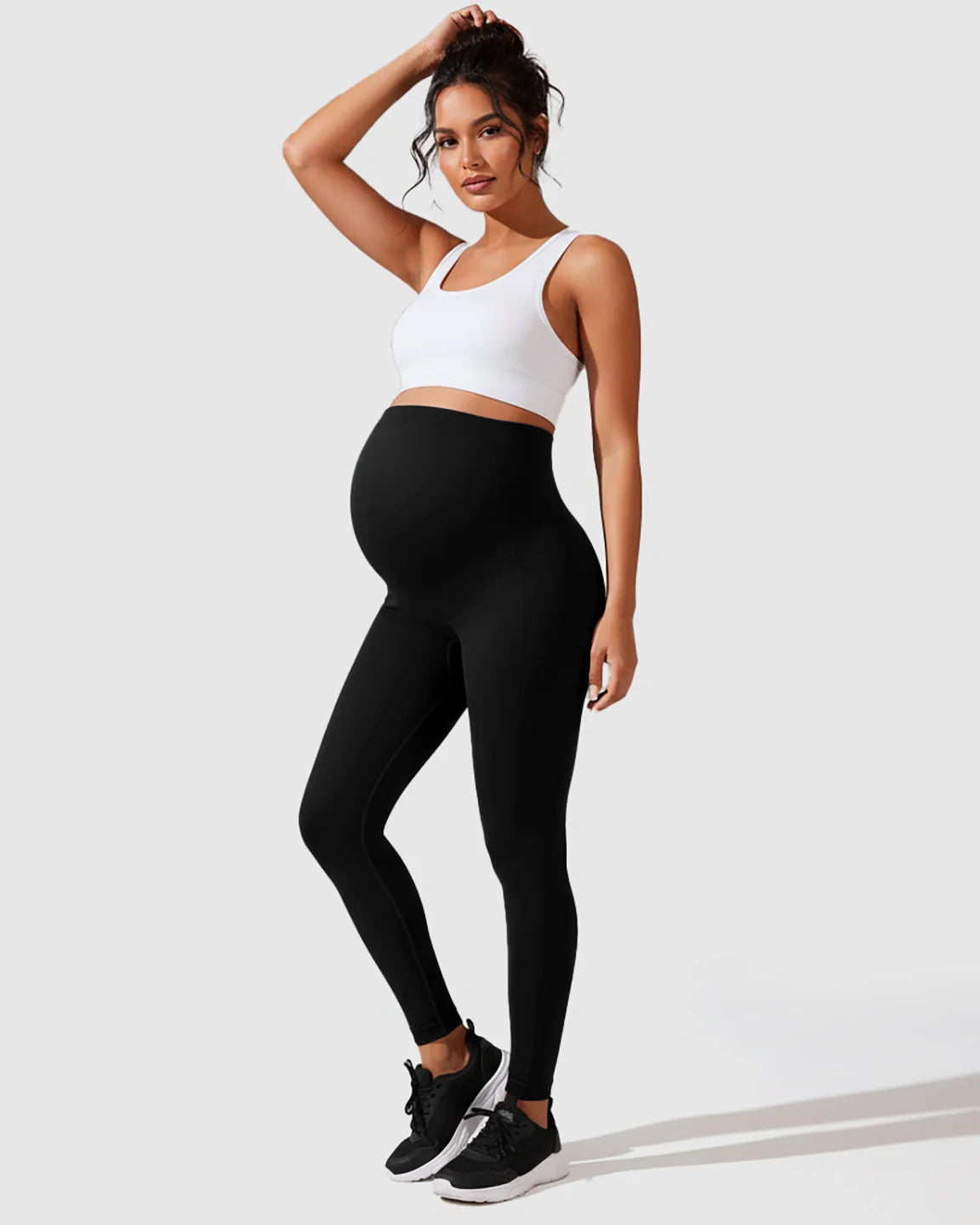 Pregnant woman in black seamless M-shape maternity leggings and white sports bra.