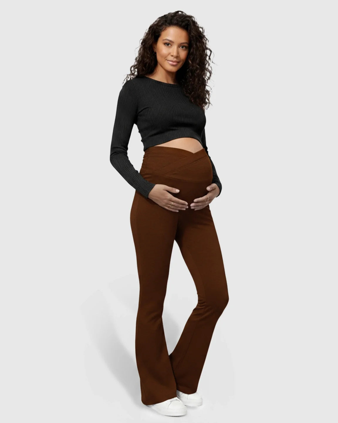 Maternity model in brown flared pants with a crossed waistband and black long-sleeve crop top.