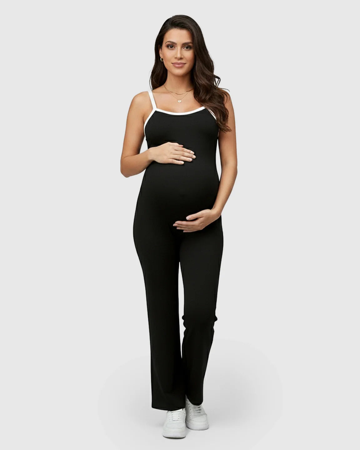 Pregnant woman in a black sleeveless maternity jumpsuit with white trim, relaxed fit, and soft stretch fabric.