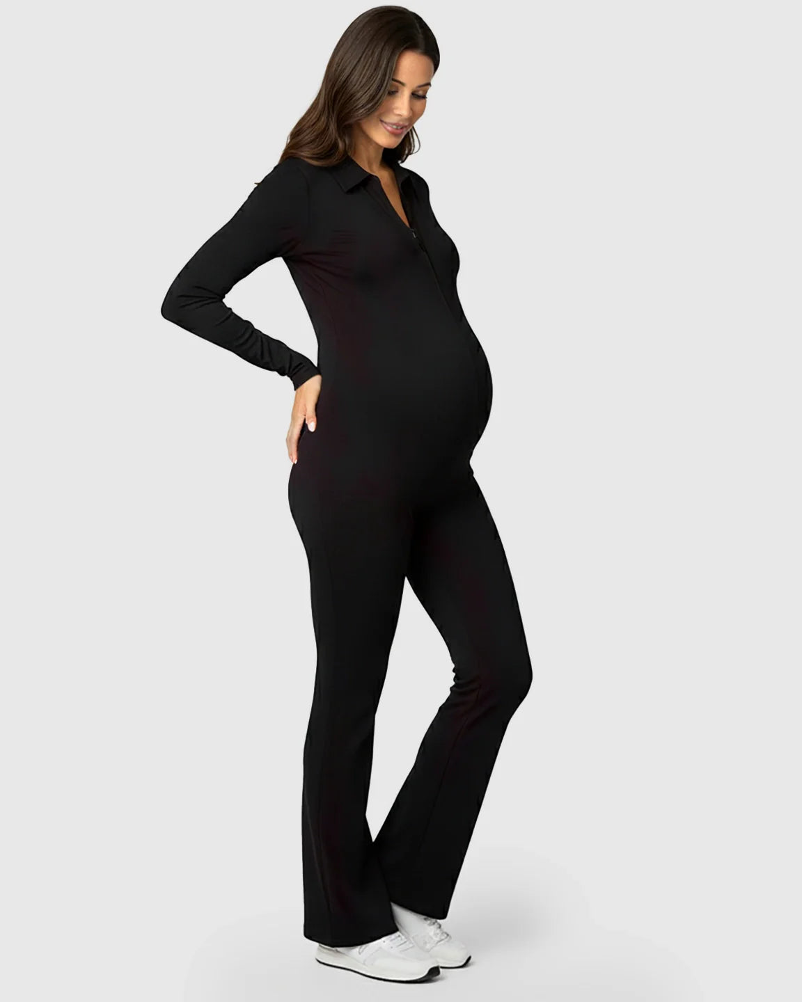 Smiling pregnant woman in a black ribbed zip-front maternity jumpsuit with flared legs.