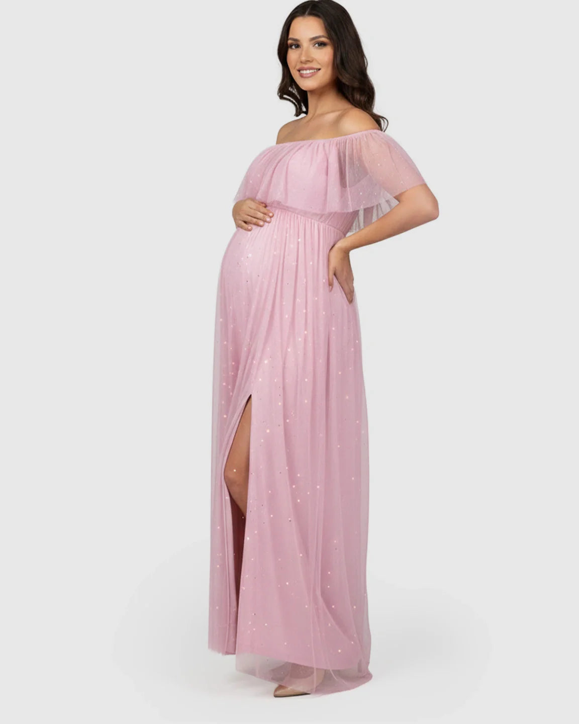 Smiling pregnant woman in a pink off-shoulder mesh maternity gown with a high slit and glitter.