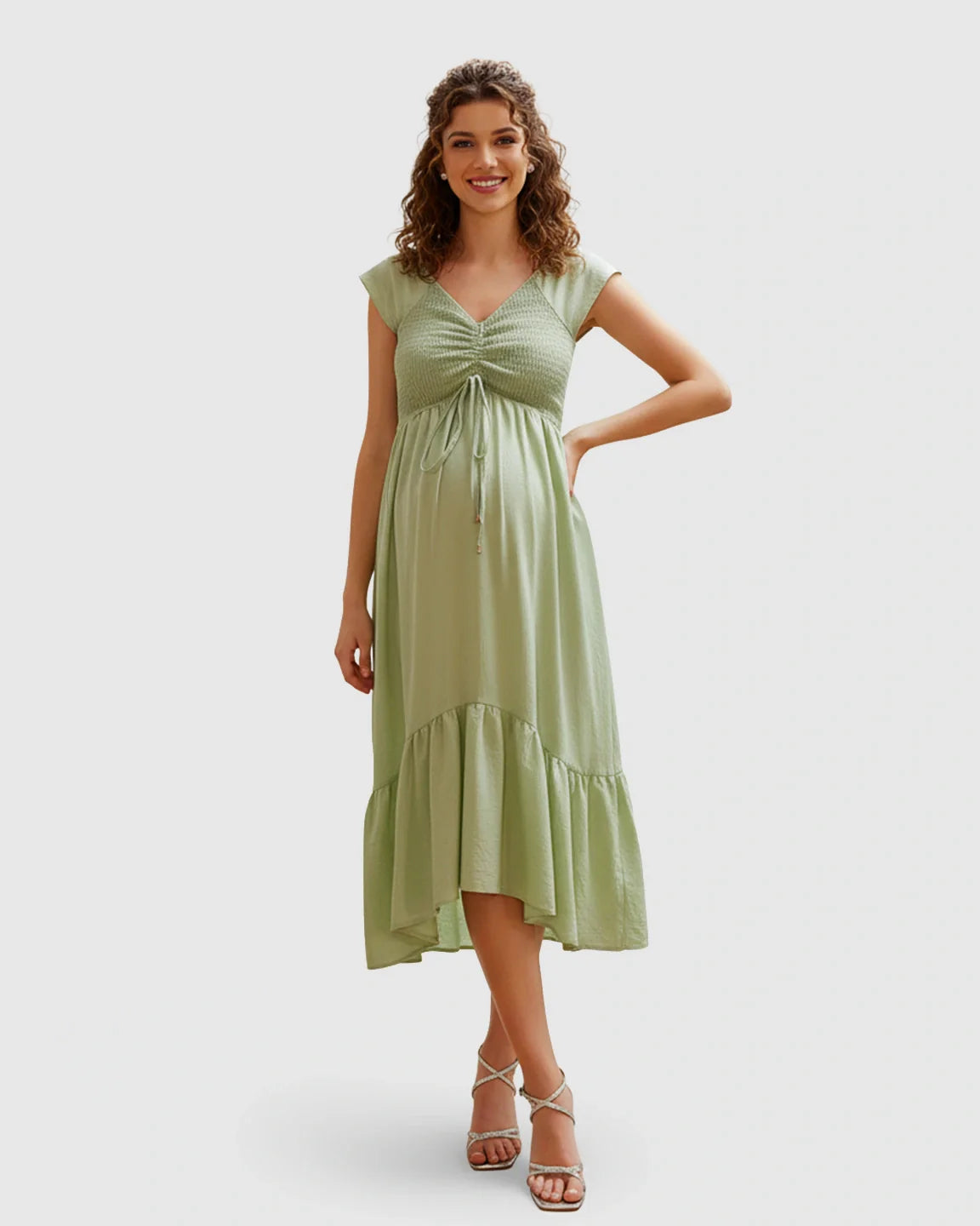 Smiling pregnant model in a sage green smocked-bodice flowy maternity midi dress with cap sleeves and V-neck.