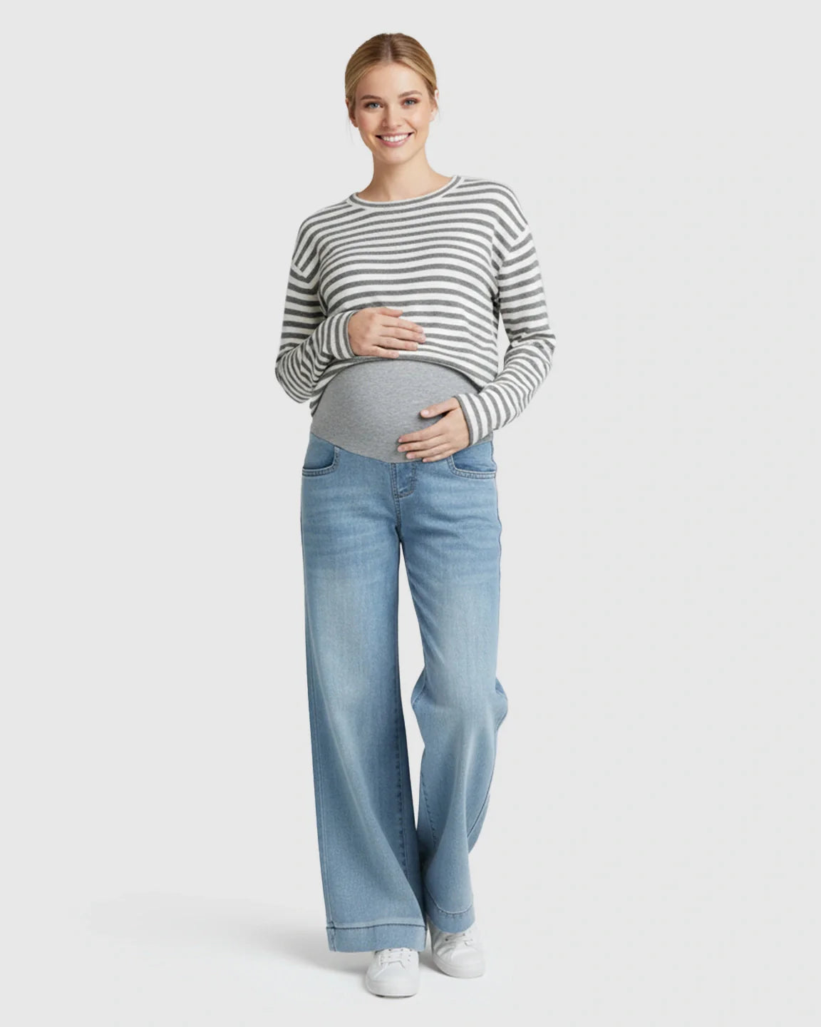 Smiling pregnant woman in light wash wide leg maternity jeans with a folded hem and grey belly band.