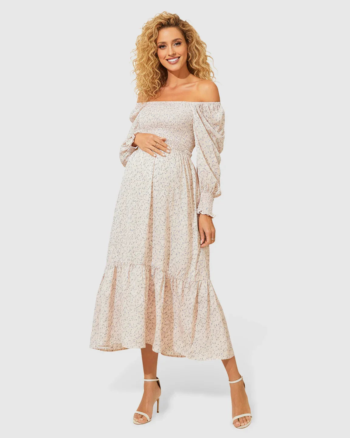Smiling pregnant woman in a flowy, off-shoulder floral maternity midi dress with smocked bodice and tiered skirt.
