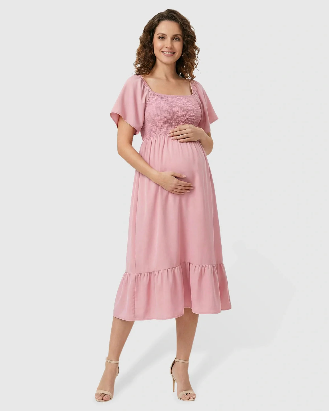 Smiling pregnant woman in a pink flutter-sleeve smocked maternity midi dress with a tiered skirt.
