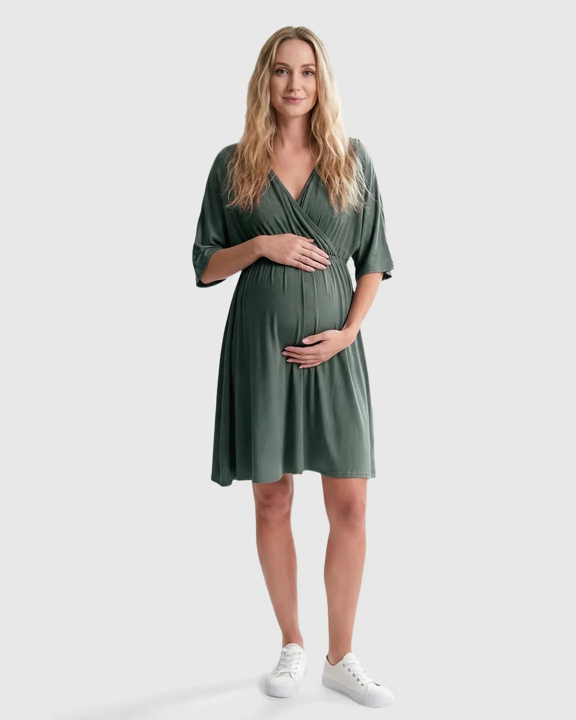 Pregnant woman in a sage green cross-front maternity midi dress with elbow-length sleeves, holding her bump.