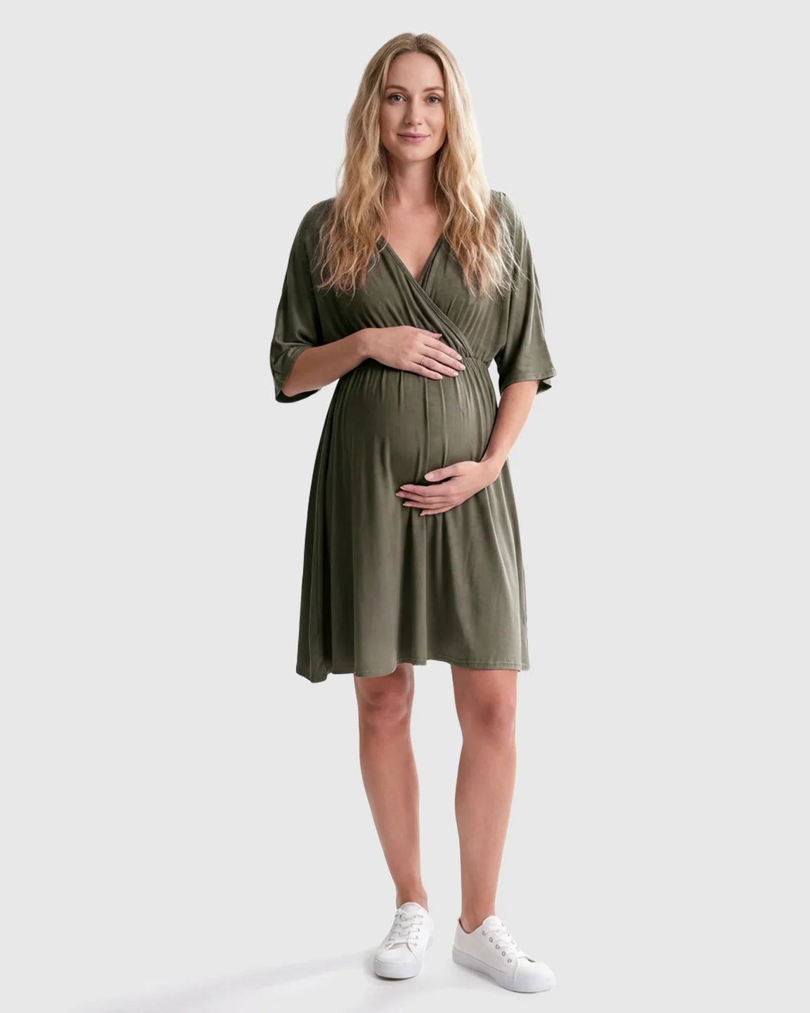 Pregnant woman in olive green cross-front maternity midi dress with 3/4 sleeves, holding her bump.