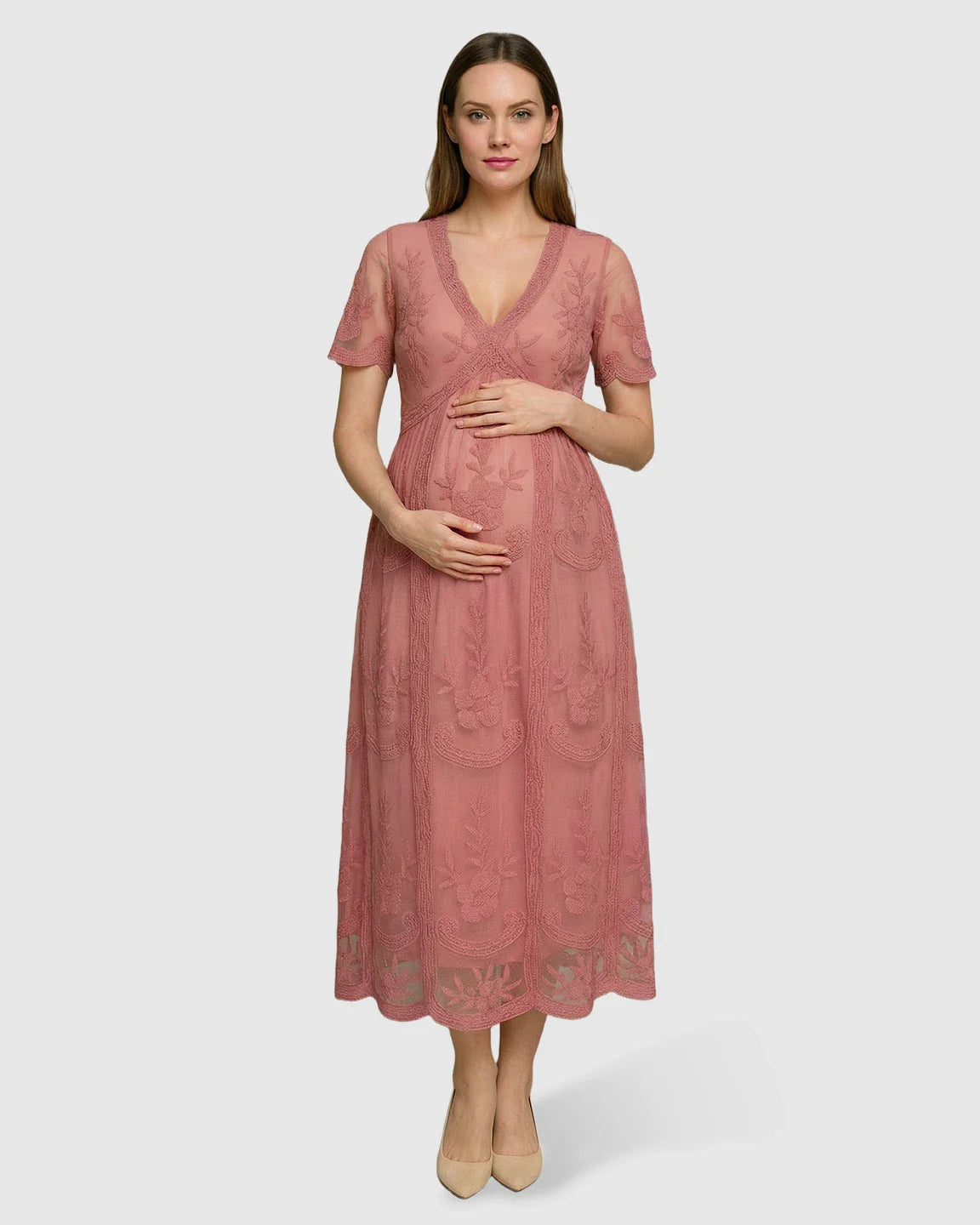 Pregnant woman in a pink lace maternity midi dress with V-neck, short sleeves, and floral embroidery.