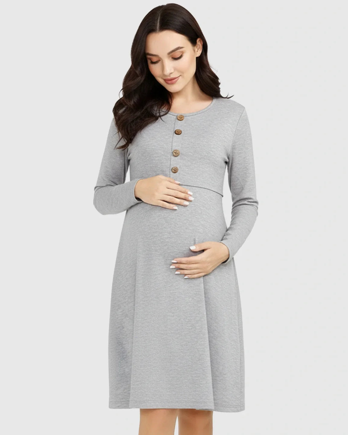Woman in a gray long-sleeve empire waist nursing dress with wood buttons, gently holding her pregnant belly.