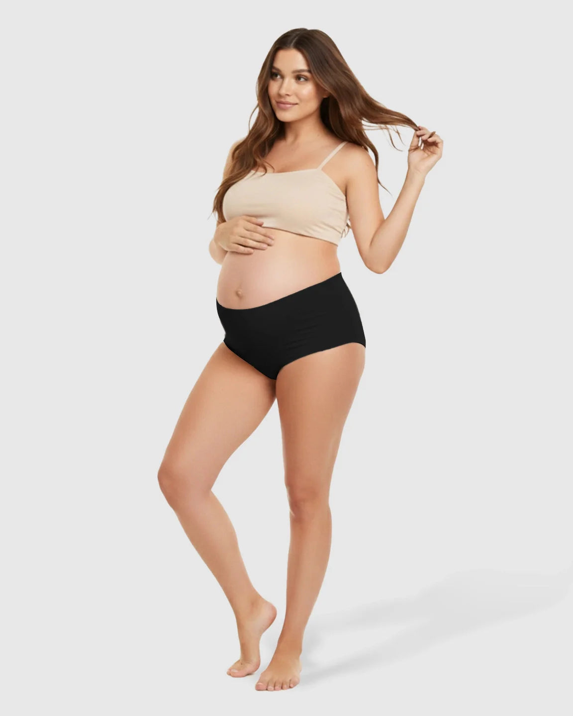 Pregnant woman wearing black seamless high-waist support maternity underwear and a nude bra, gently touching her belly.