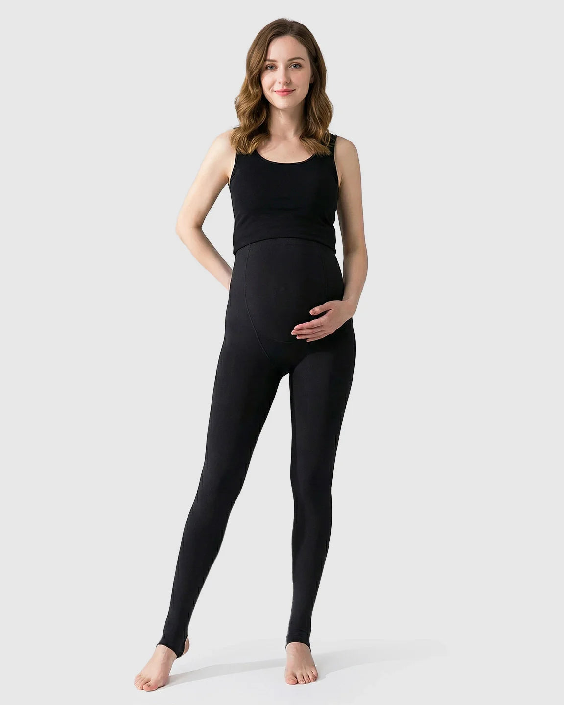 Smiling pregnant woman wearing black fleece-lined over-bump maternity leggings with stirrups and a black tank top.