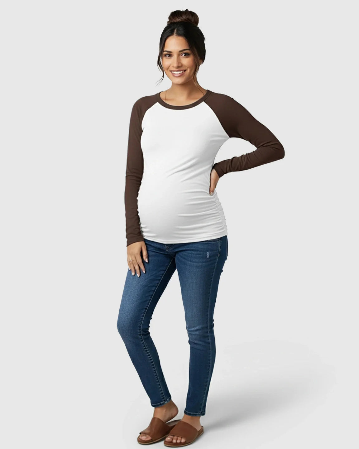 Smiling pregnant woman in a white and brown raglan sleeve maternity top with ruched sides and blue jeans.