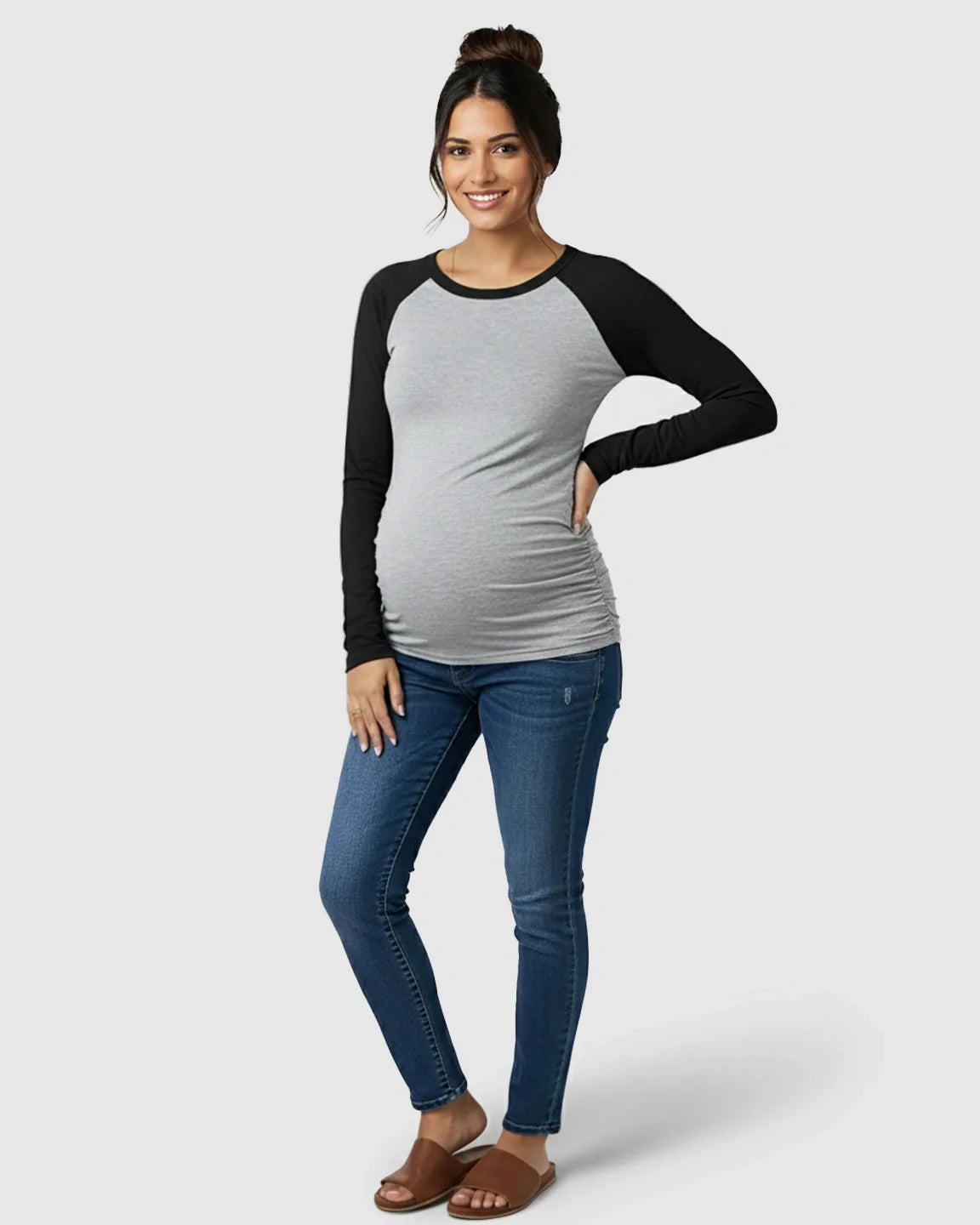 Smiling pregnant woman in a gray and black raglan sleeve maternity top with side ruching and blue jeans.