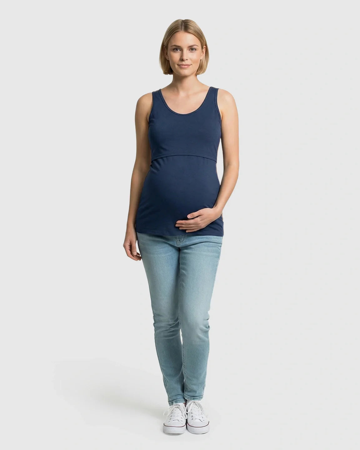 Blonde pregnant model wearing a navy blue stretch nursing-access maternity tank top and light wash jeans.