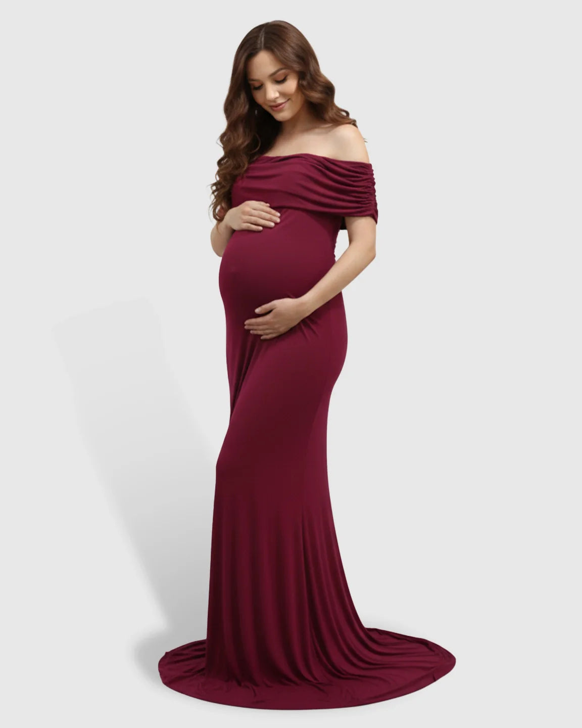 Pregnant woman in a burgundy off-shoulder bodycon mermaid maternity gown, cradling her bump.