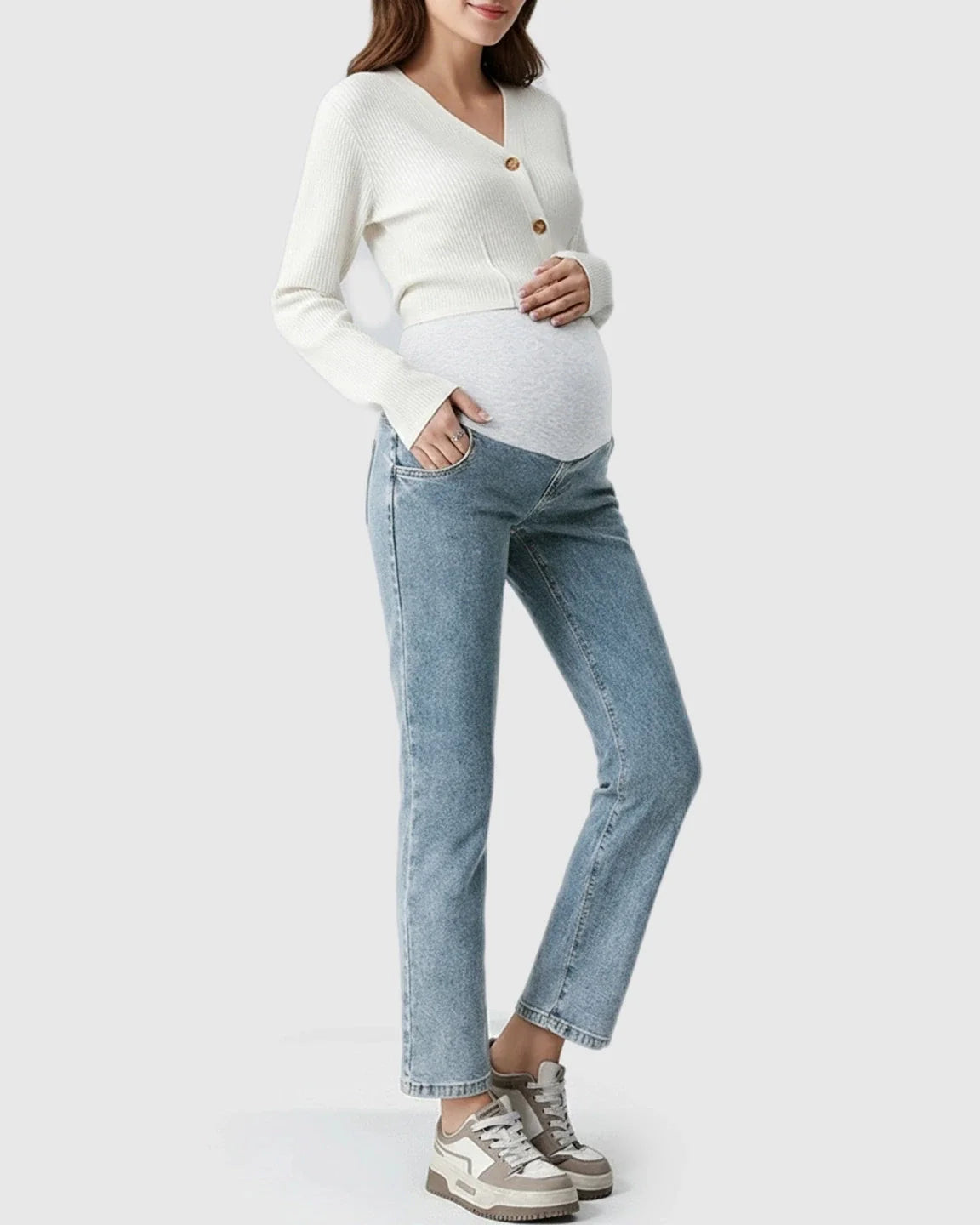 Pregnant woman in light wash stretch denim straight-leg maternity jeans with a grey belly band and white cardigan.