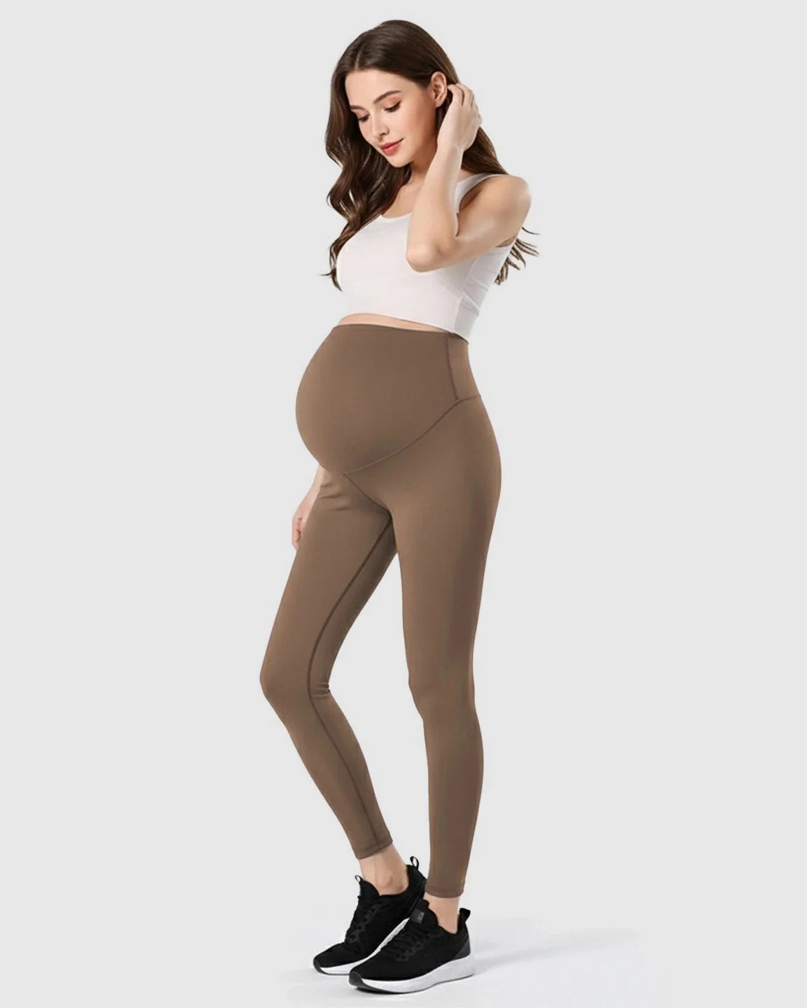 Woman models brown double-layer belly support maternity leggings with a white crop top.