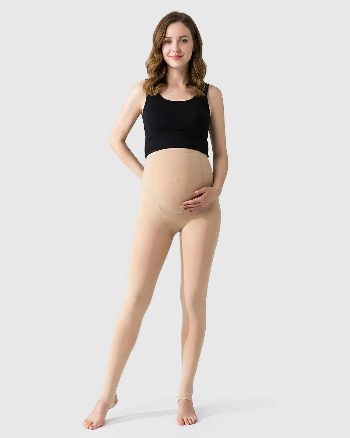 Smiling pregnant woman in nude fleece-lined over-bump maternity leggings with stirrups and a black tank top.