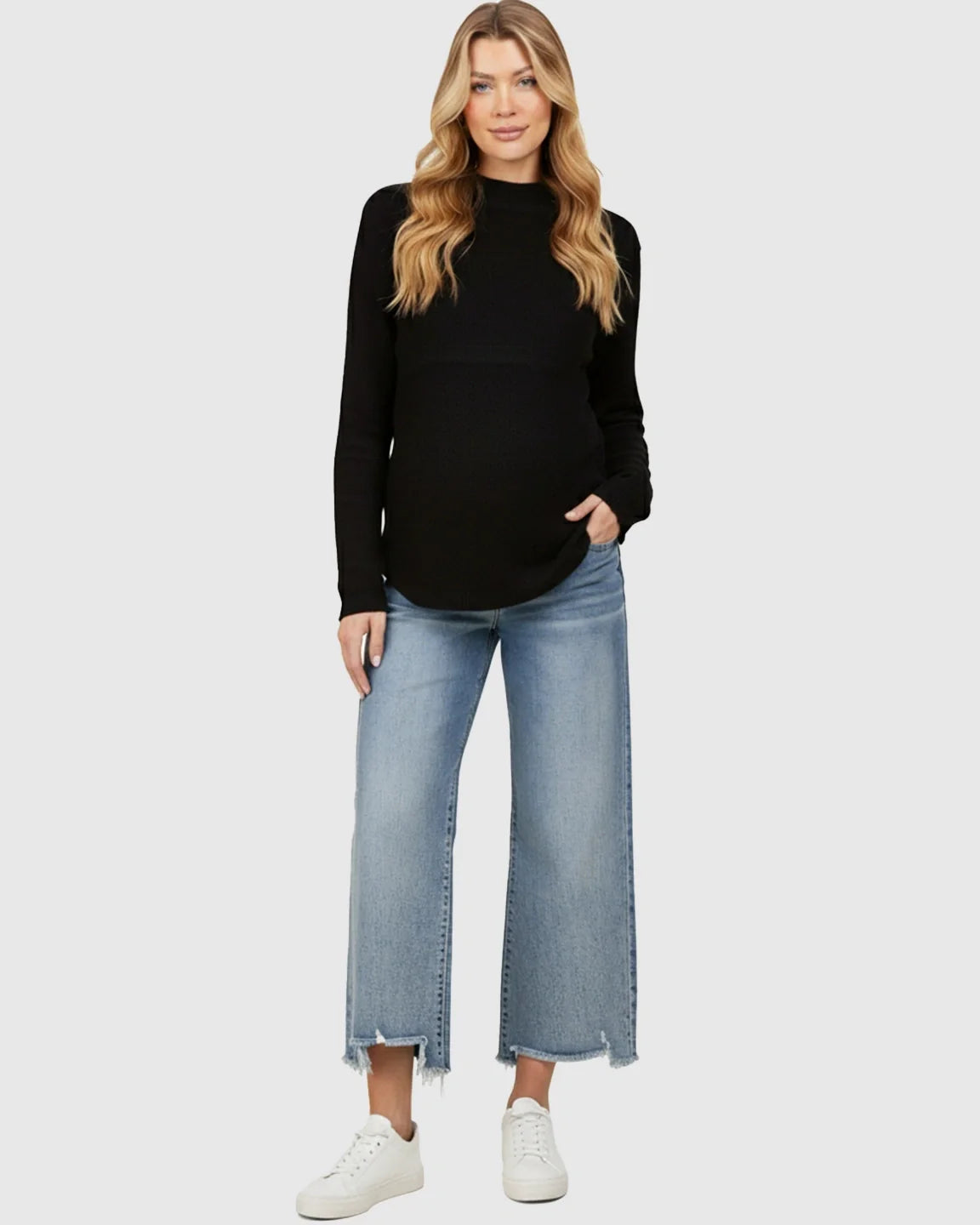 Woman in black long-sleeve top and light wash wide-leg maternity jeans with raw hems.