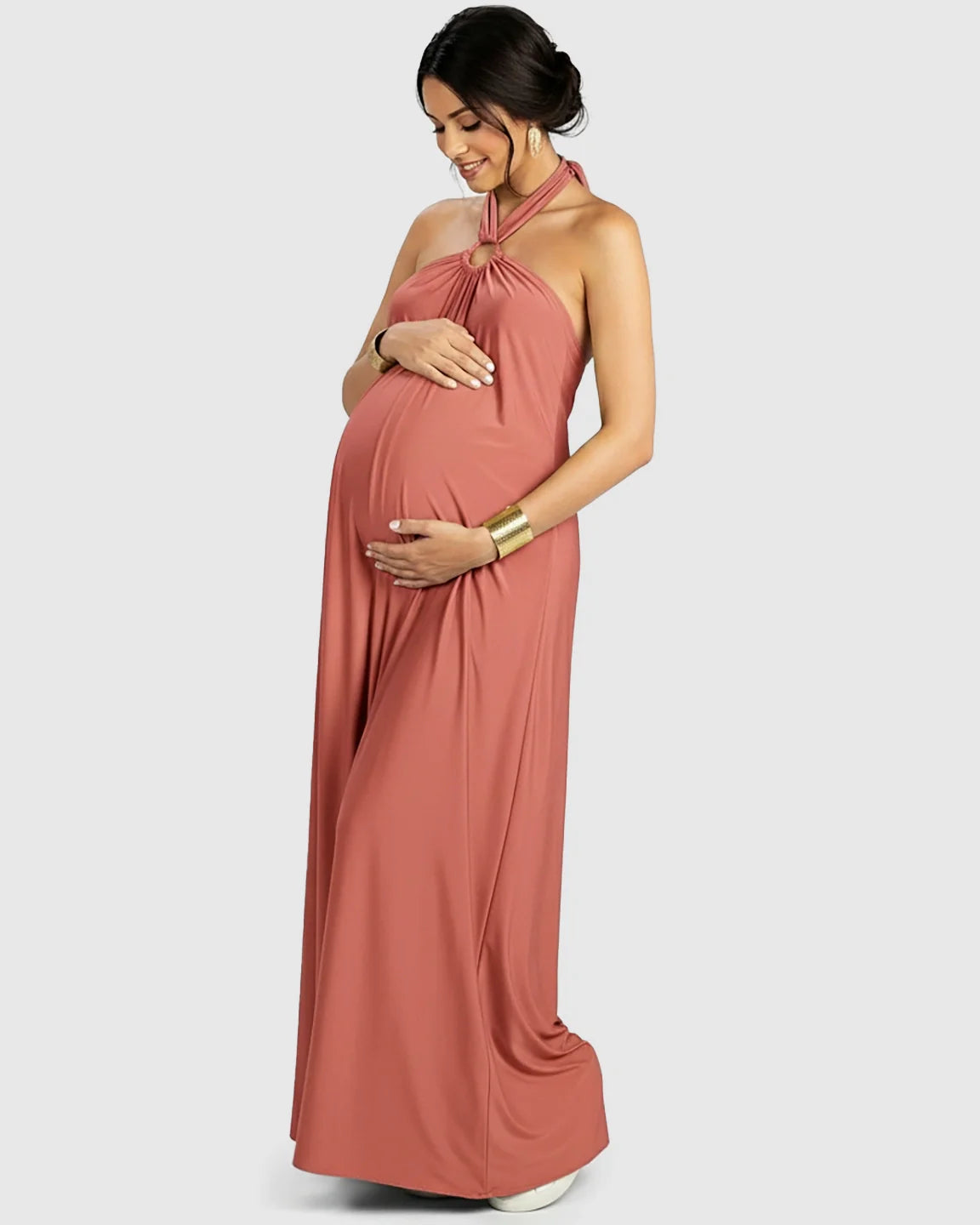 Pregnant woman in a flowing terracotta backless halter neck chiffon maternity maxi dress.