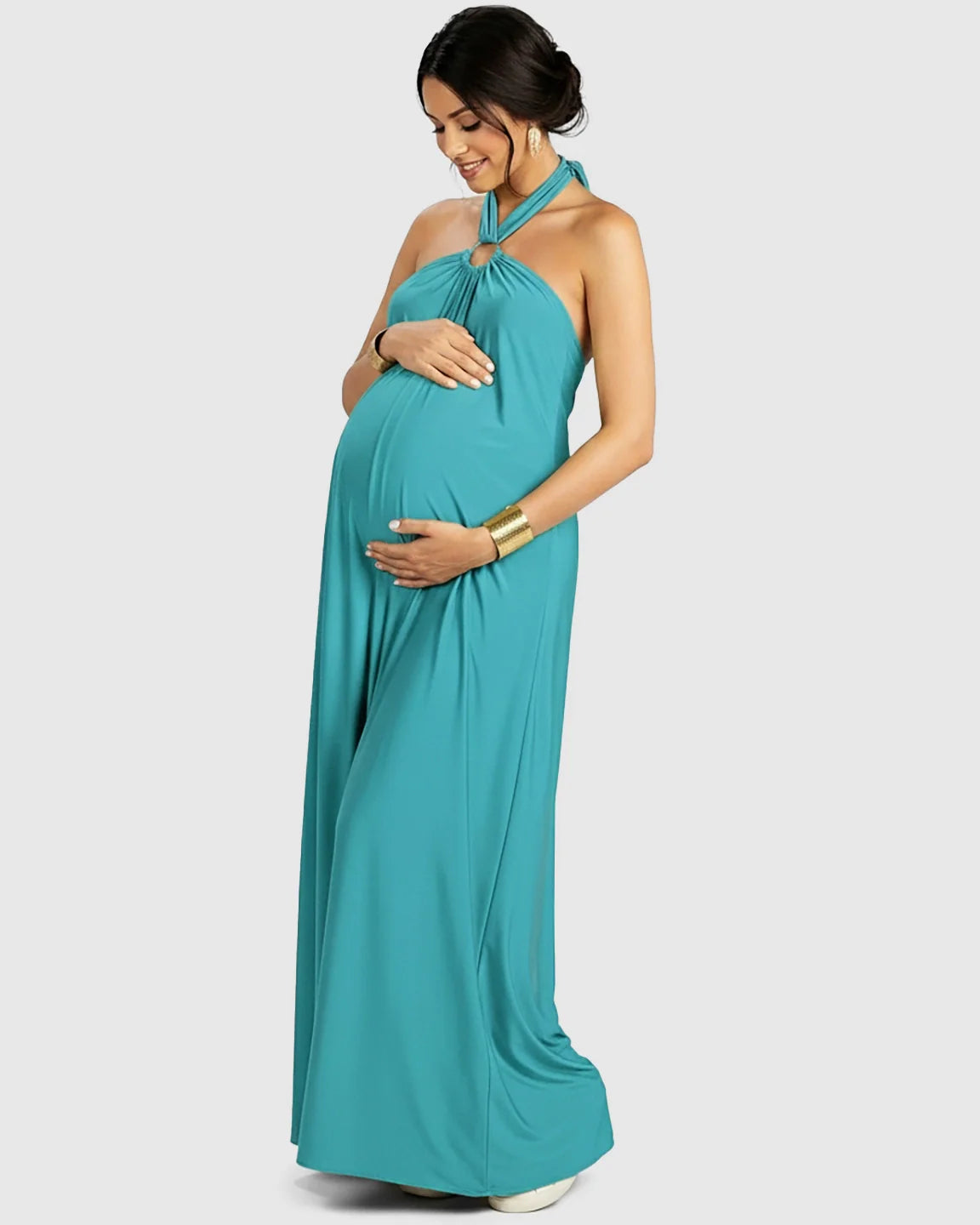 Pregnant woman in a teal backless halter neck chiffon maternity maxi dress, smiling and holding her bump.
