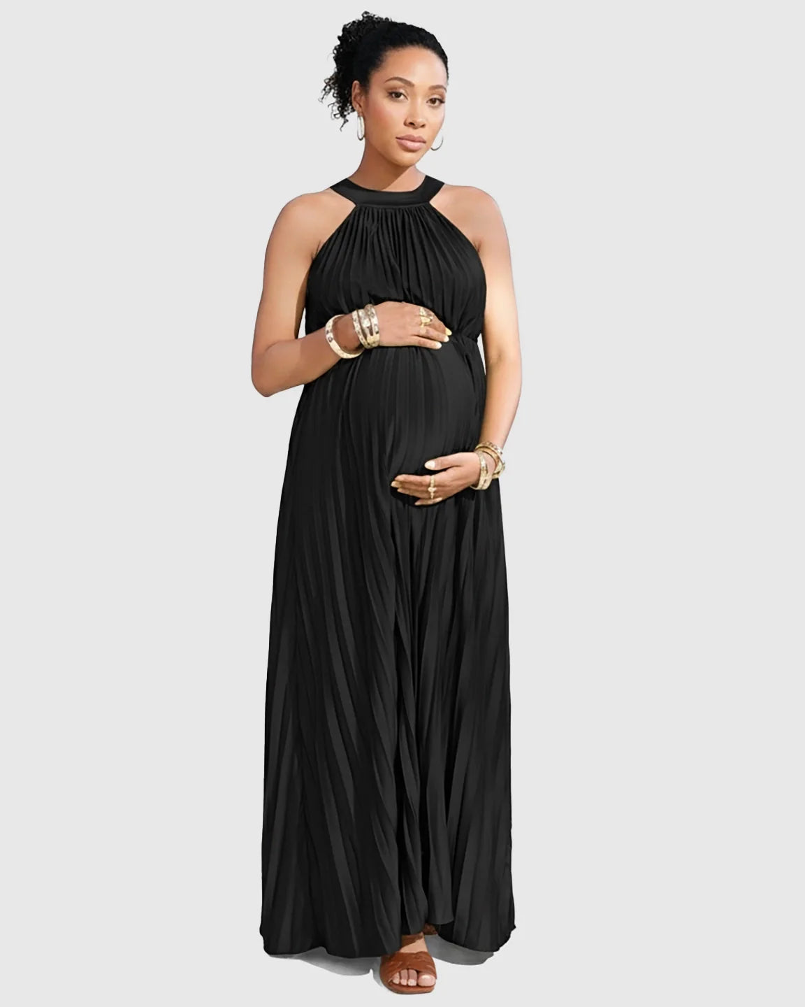 Pregnant woman in a black faux silk halter neck pleated maternity maxi dress, holding her belly.