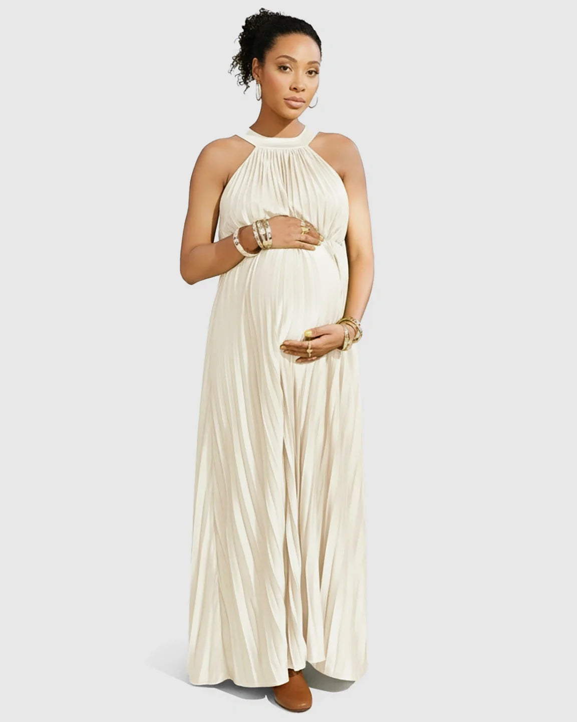 Pregnant woman in a flowing ivory faux silk halter neck pleated maternity maxi dress.