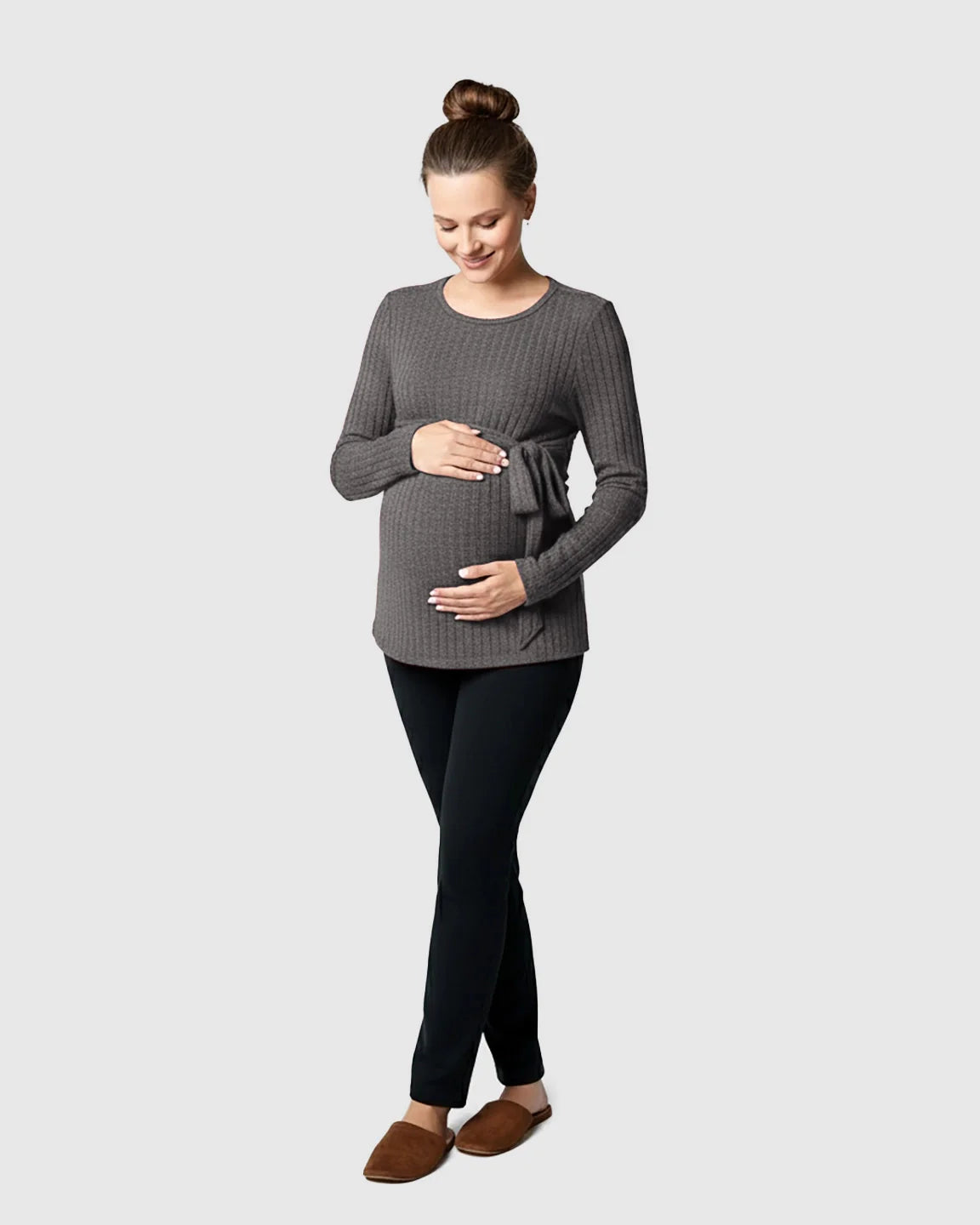 Pregnant woman smiling in a gray ribbed tie-waist long sleeve maternity sweater and black pants.
