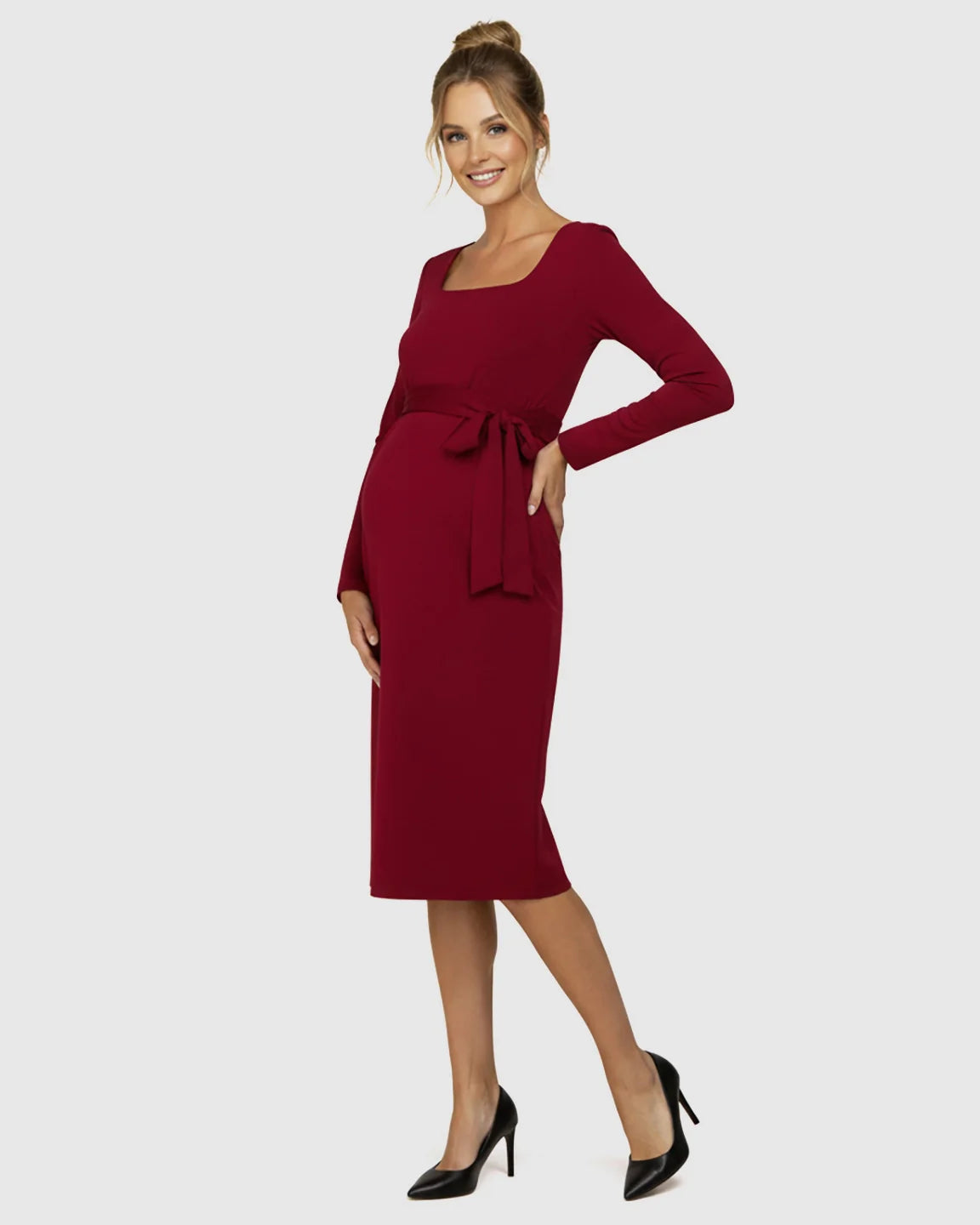 Smiling pregnant model in a red square neck, long-sleeve bodycon maternity midi dress with side-tie.