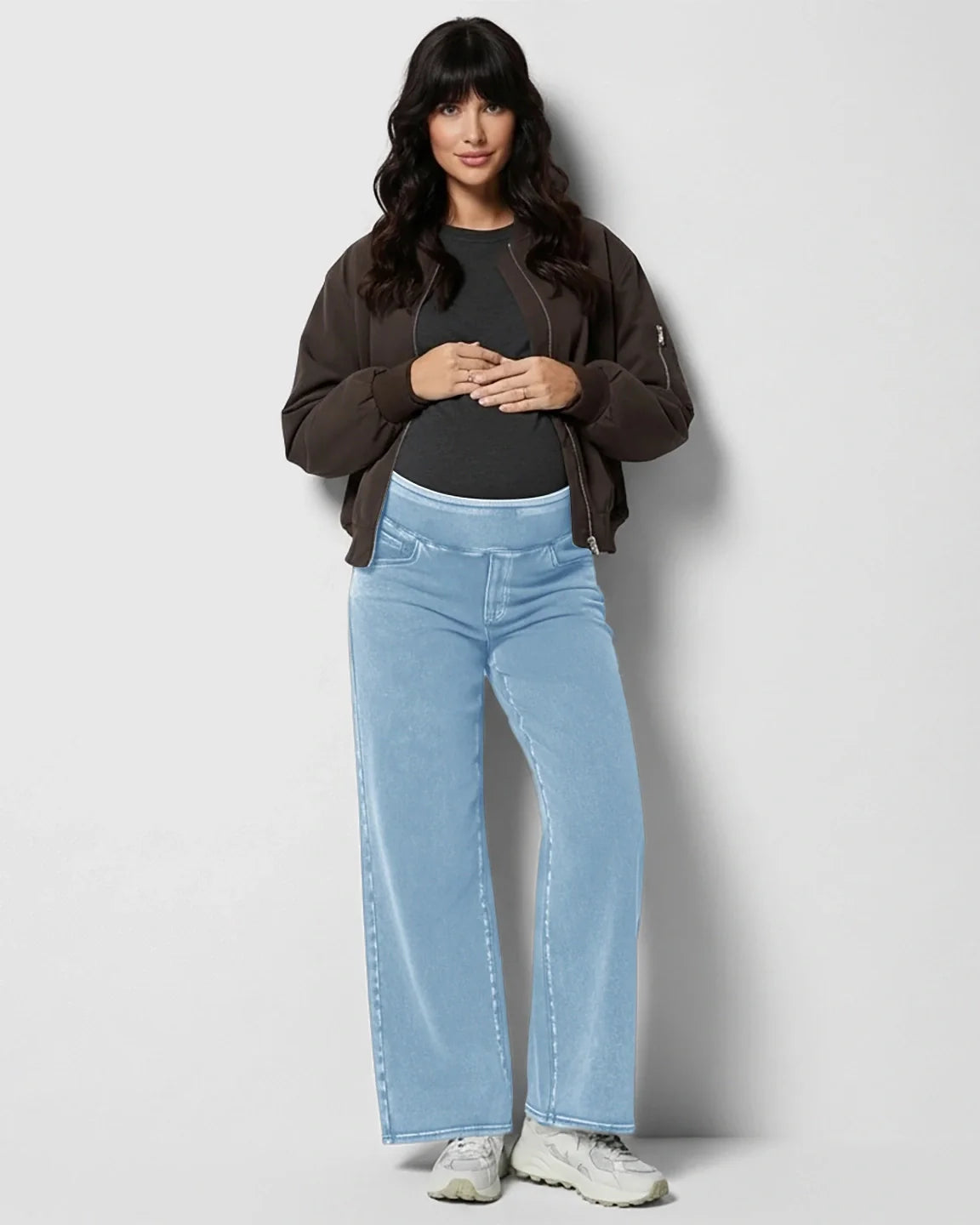 Woman modeling light blue wide-leg maternity denim jeans with a soft waistband, paired with a dark top and bomber jacket.