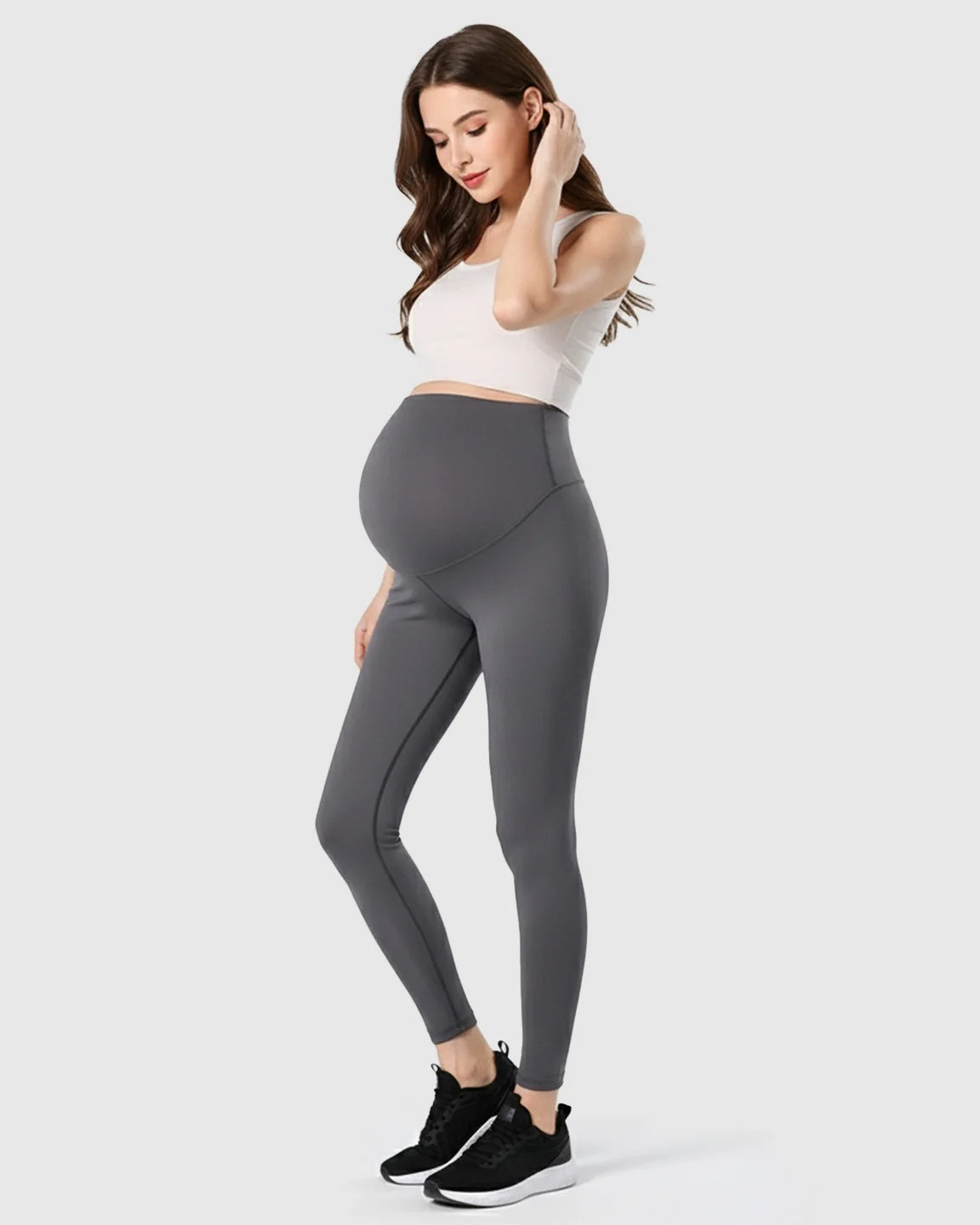 Woman in charcoal gray double-layer belly support maternity leggings and white crop top.