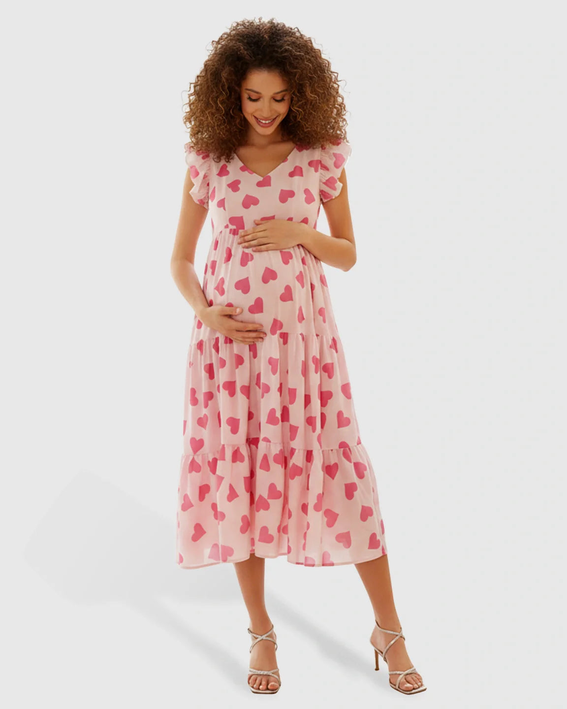 Pink chiffon maternity midi dress with red heart print, tiered skirt, V-neck, and flutter ruffle sleeves.