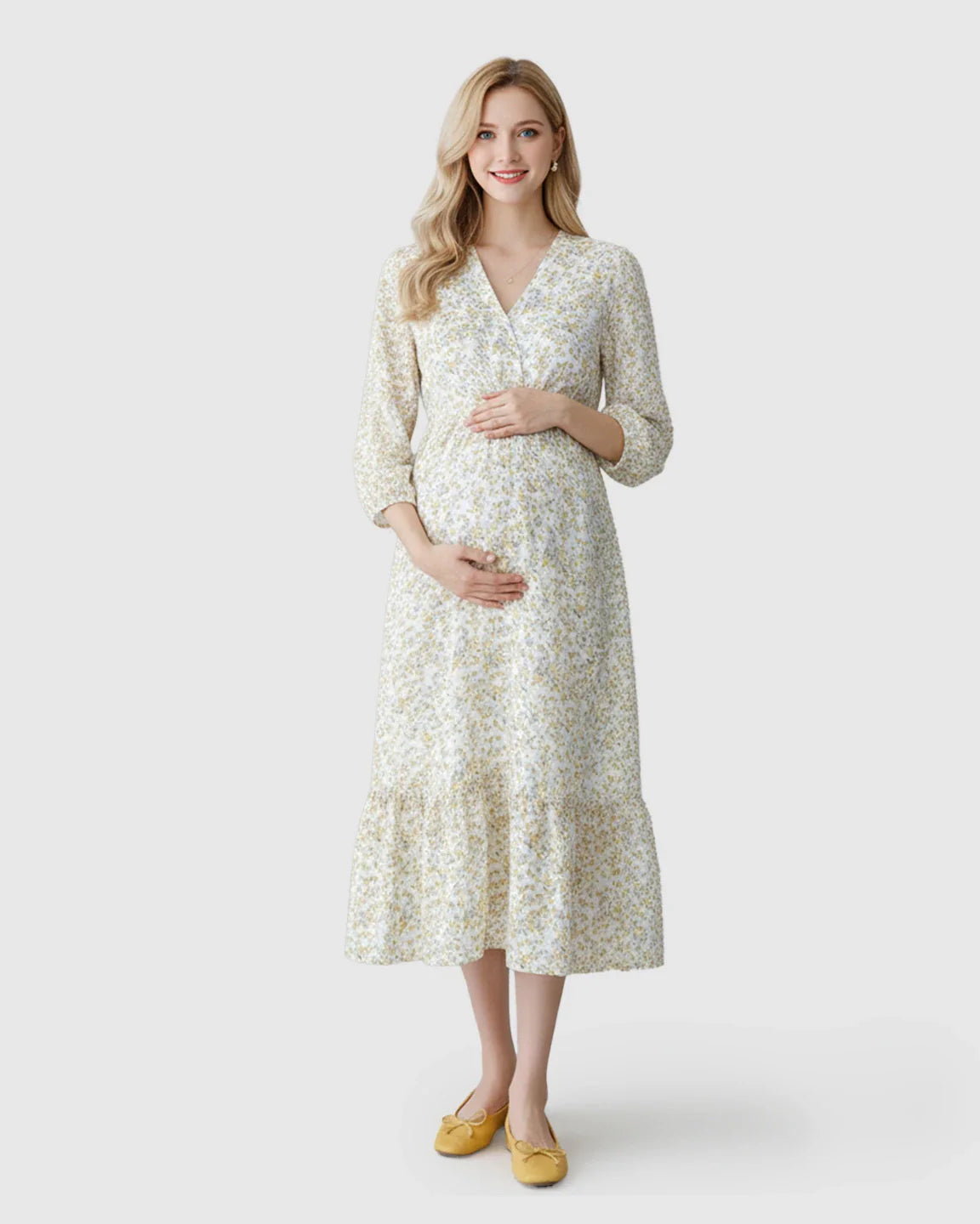 Blonde pregnant woman in a white floral ruffle hem smocked waist maternity midi dress with yellow flats.