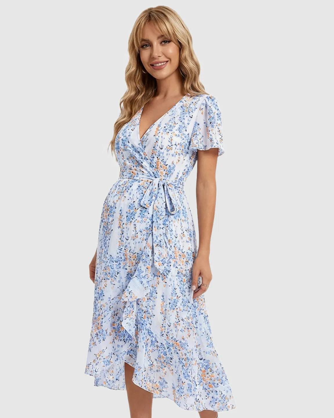 Blonde pregnant woman in a white floral V-neck ruffled hem maternity midi dress with a tie waist.