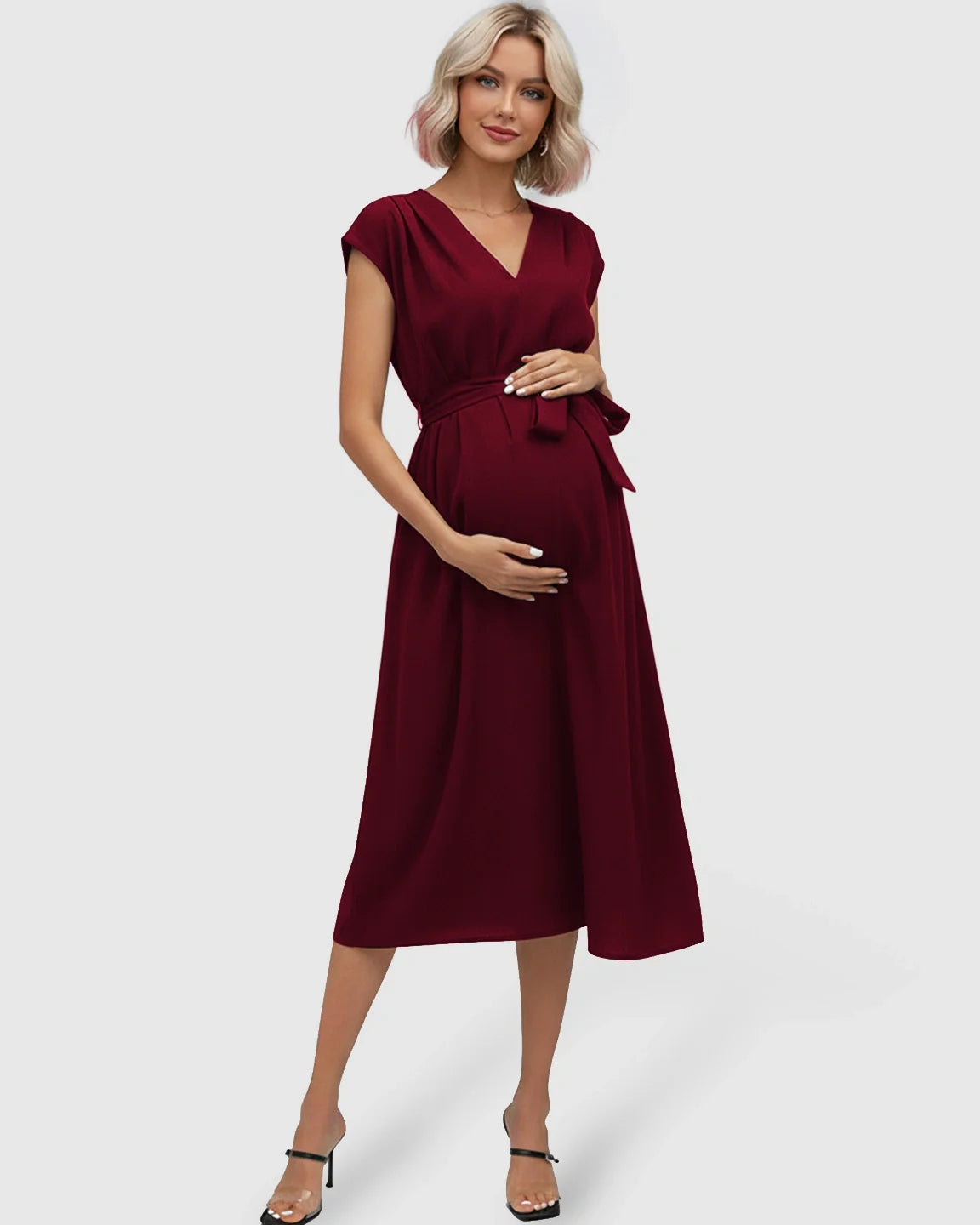 Maternity midi dress in deep red with V-neck, flutter sleeves, and adjustable tie-waist, worn by a pregnant woman.