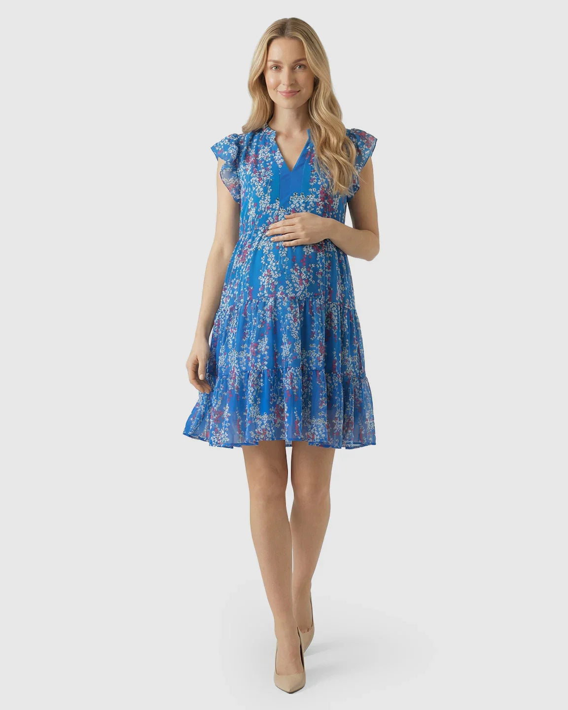 Smiling pregnant woman in a blue floral chiffon V-neck A-line maternity dress with flutter sleeves.