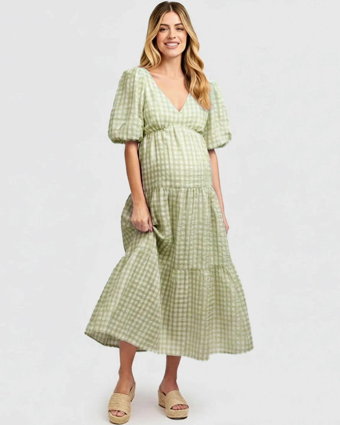 Smiling pregnant woman in a light green checkered maternity maxi dress with puffed sleeves and a V-neck.