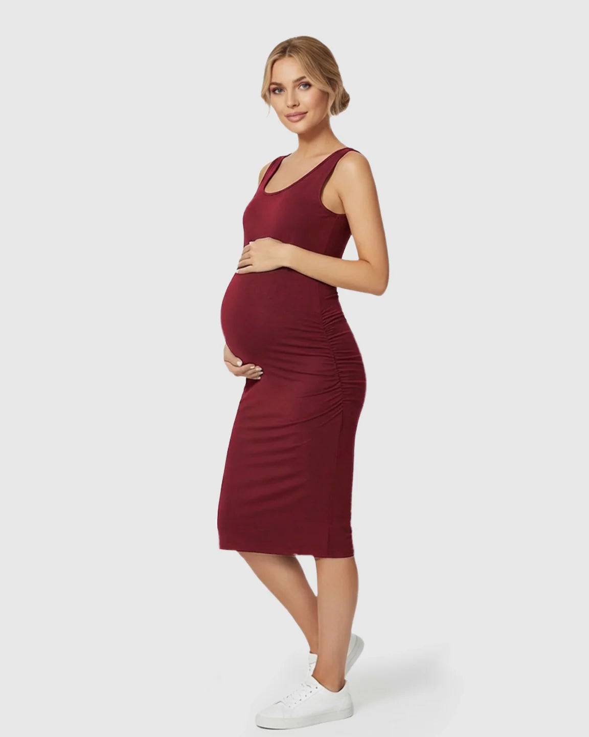 Pregnant woman in a maroon sleeveless bodycon maternity dress with side ruching, paired with white sneakers.